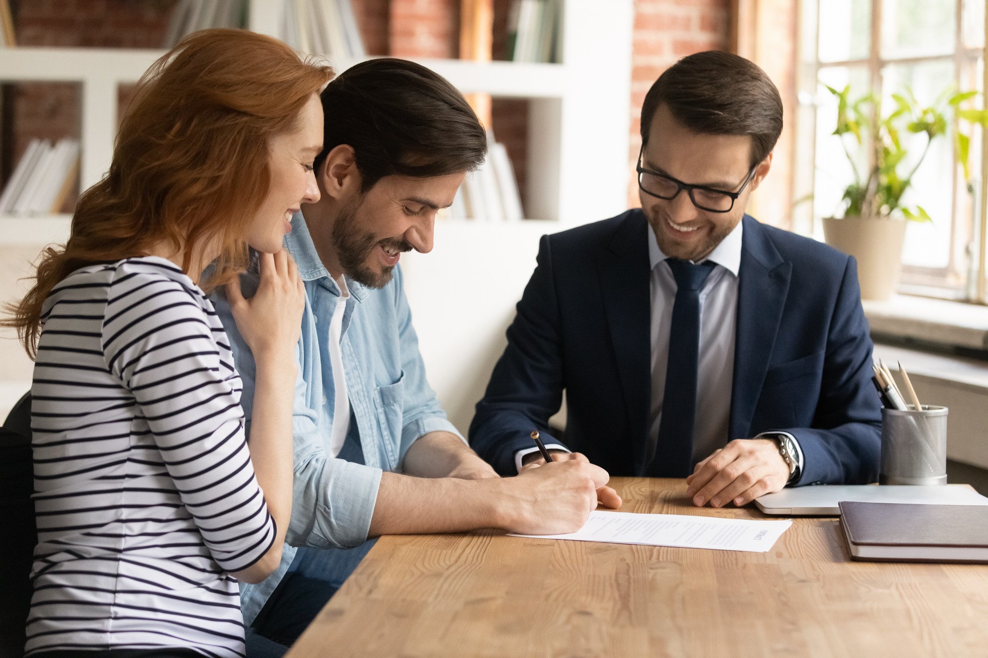 Happy millennial couple signing contract with manager at meeting